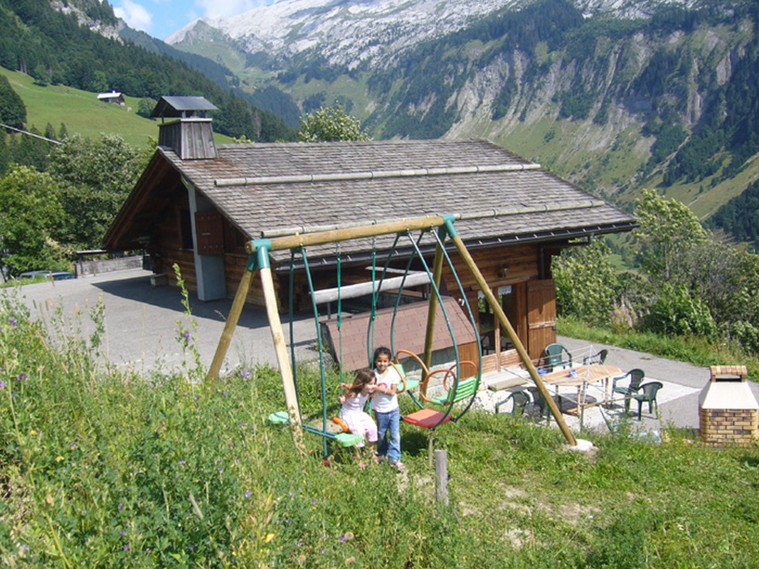 Vue en &eacute;t&eacute; avec son espace jeux (balan&ccedil;oire) et sa terrasse (mobilier de jardin, store &eacute;lectrique, barbecue)